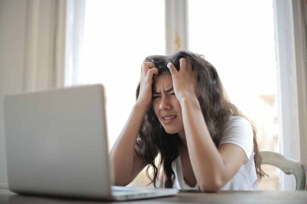 Female high school student in a white t-shirt pulling at her hair and looking frustrated in front of her laptop.